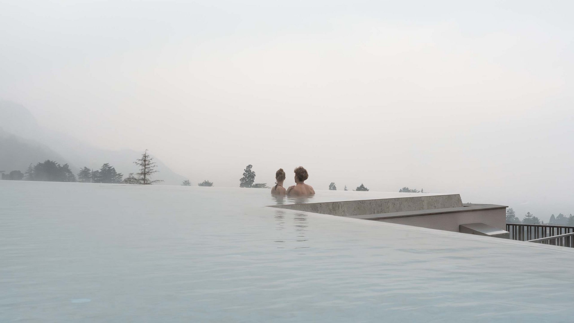 Zwei Personen in einem Infinity-Pool mit nebliger Berglandschaft im Hintergrund